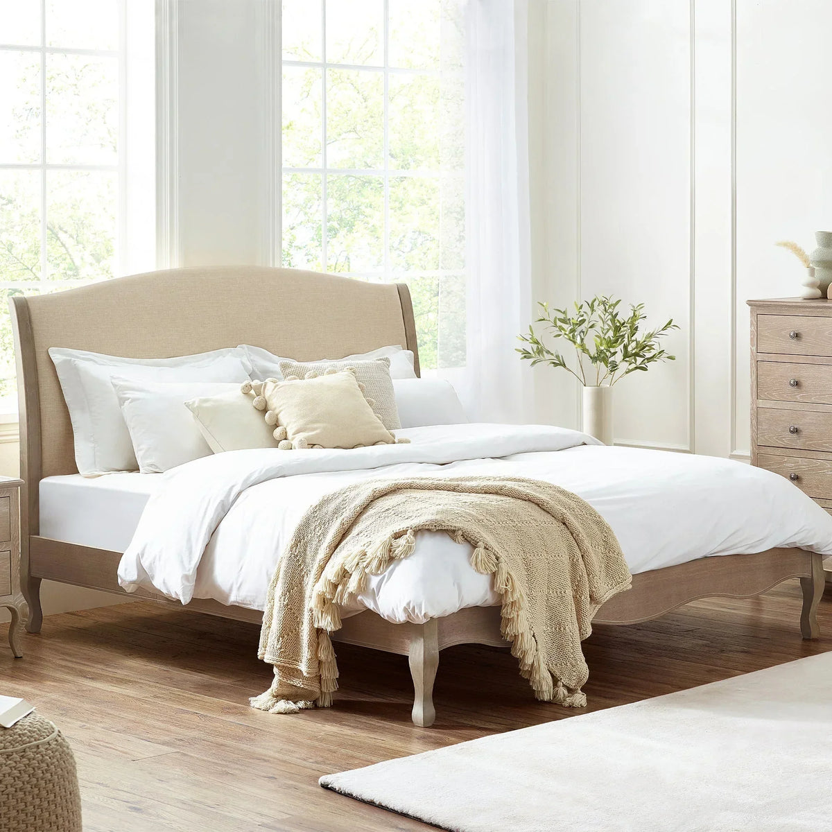 Beige double bed with upholstered headboard, white bedding and throw in bright bedroom