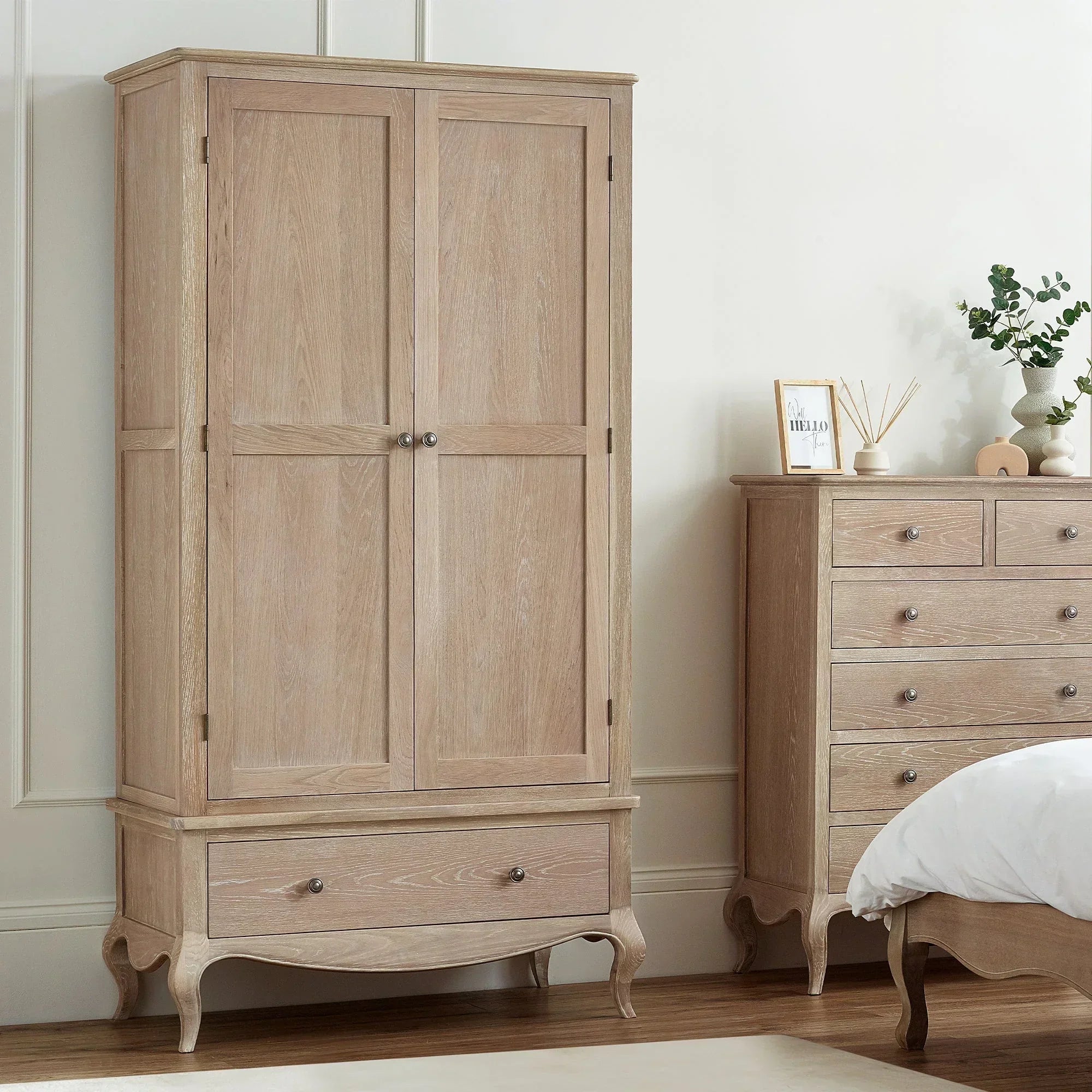 Light oak wardrobe with lower drawer beside matching chest of drawers in bedroom setting