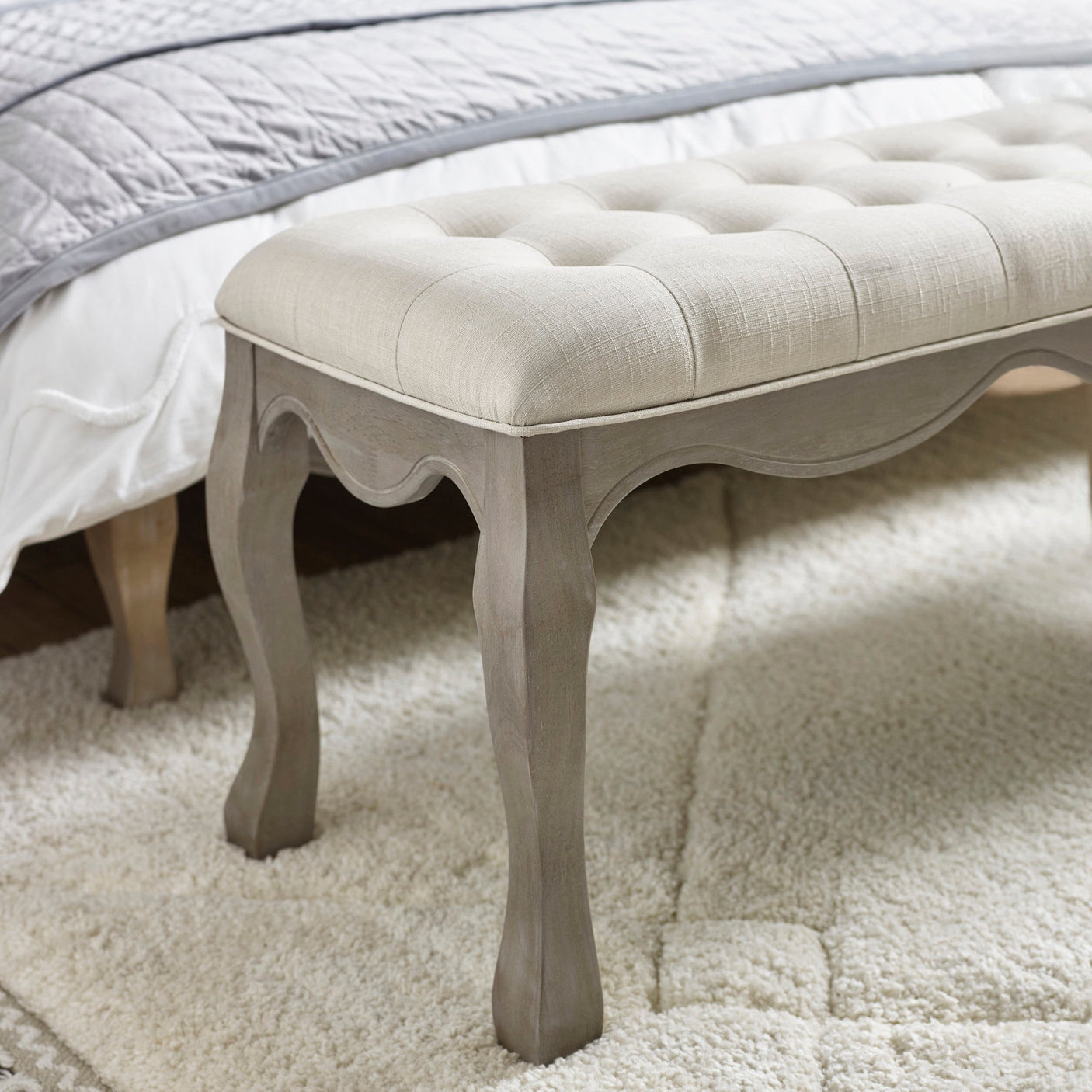 Close up of bench leg and curved apron in natural wood with button tufted beige fabric edge