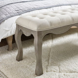 Close up of bench leg and curved apron in natural wood with button tufted beige fabric edge