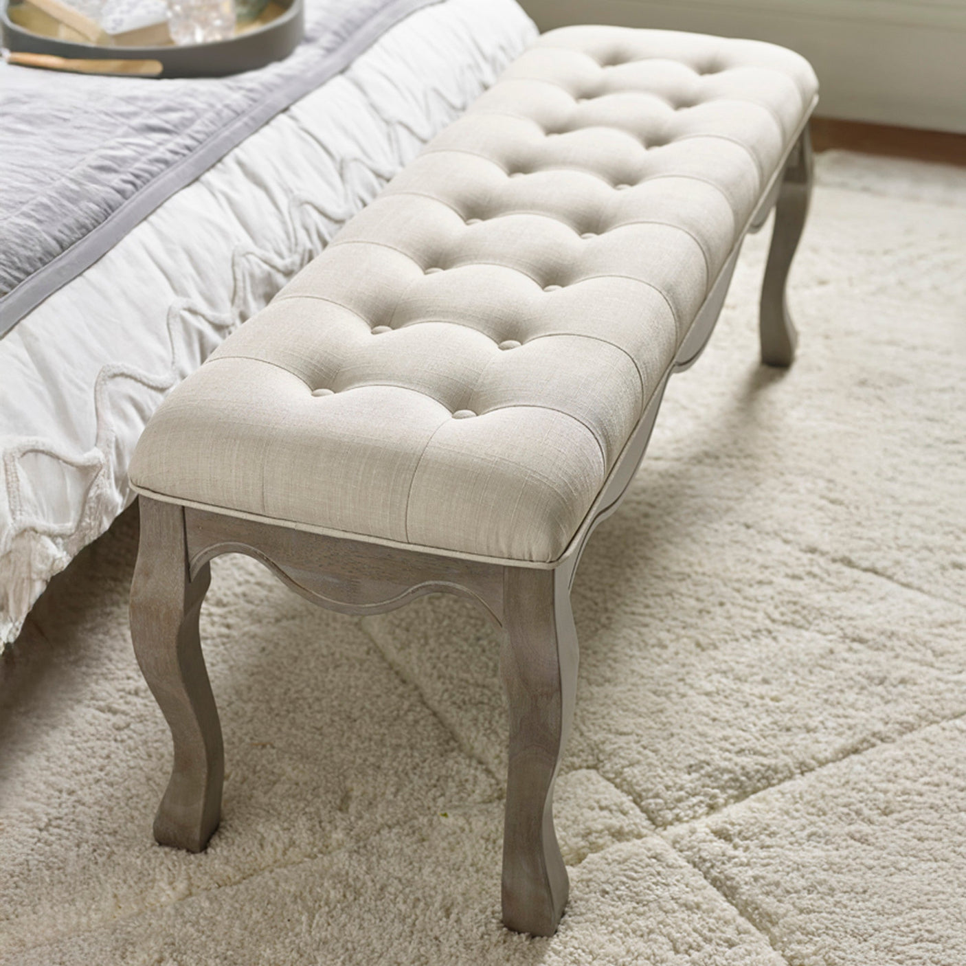 Angled top view of beige button tufted fabric bench with natural wood cabriole legs on cream rug