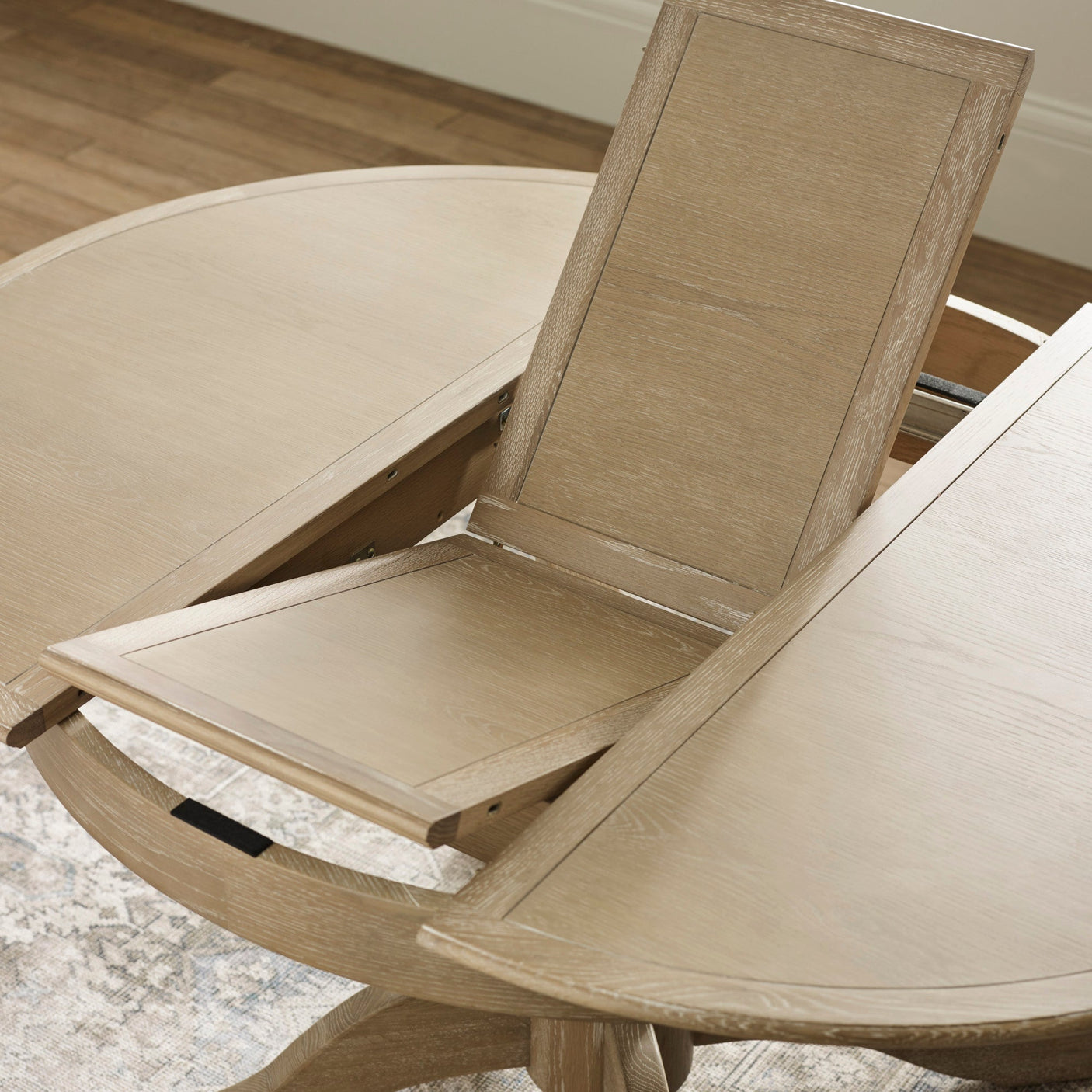 Light oak round extending table with leaf insert partially lifted showing extension mechanism