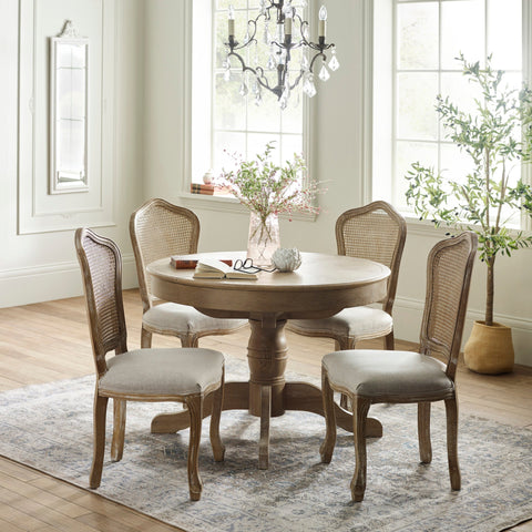 Round extending wooden dining table with four beige cushioned cane-back chairs in bright room