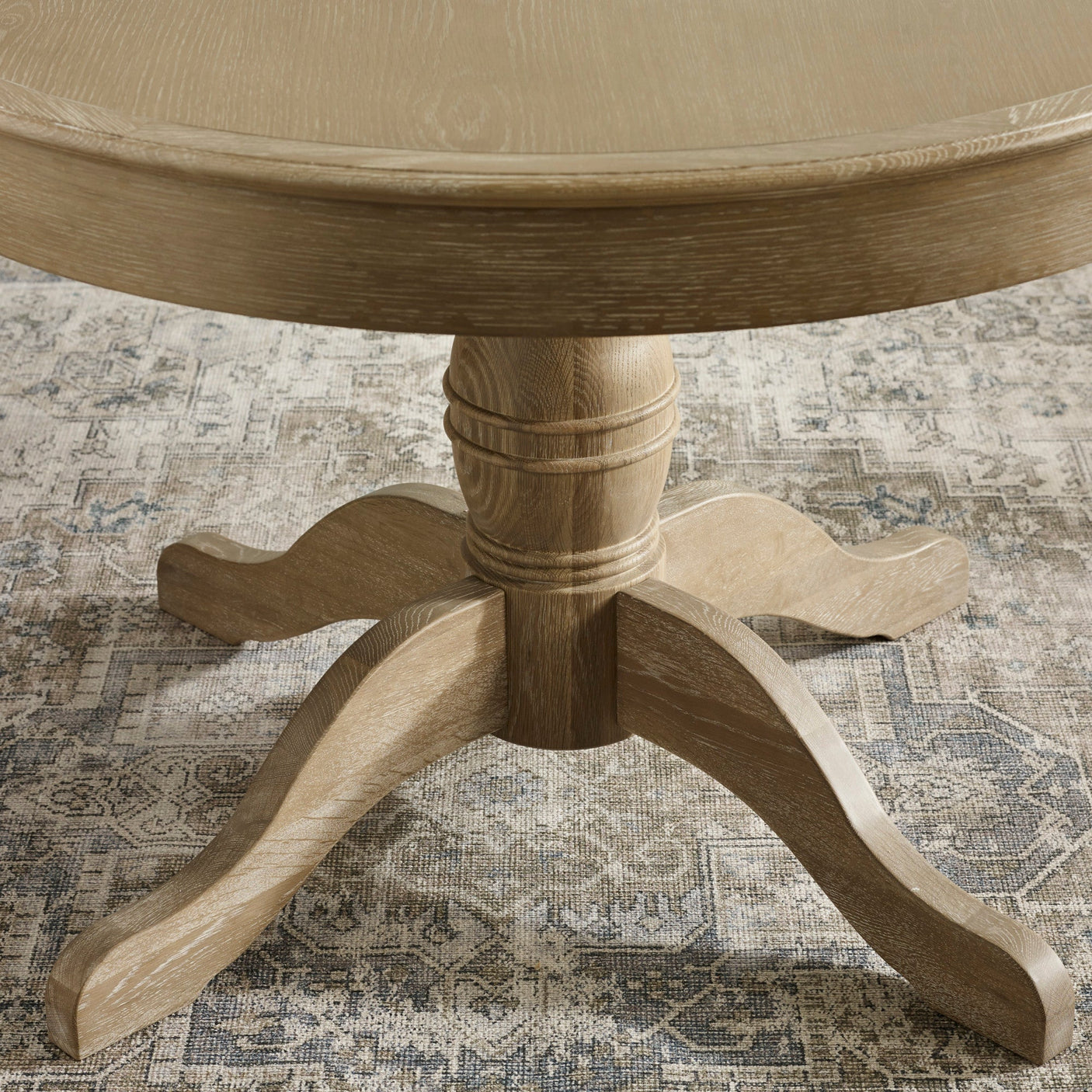 Close-up of pedestal table base with four curved feet in light brown wood on patterned rug