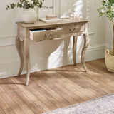 The Camille Console Table in limed oak features elegant curved legs and two drawers, set against a softly lit room with a neutral color palette and decorative accents
