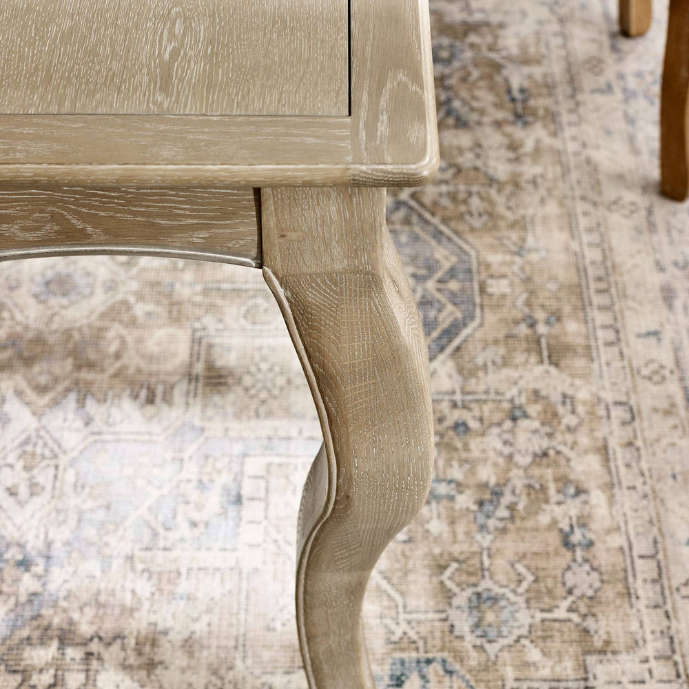 The Camille French Style Rectangular 4-6 Seater Extending Dining Table features a limed oak finish with elegantly curved legs, set against a patterned area rug that enhances its classic charm