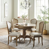 Four Camille dining chairs around round pedestal table with light cushions and wood grain finish in light room