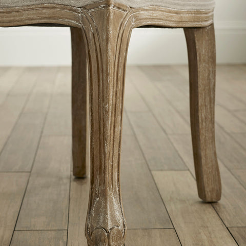 Close-up of carved wooden leg with weathered finish and light beige fabric on seat edge