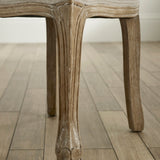 Close-up of carved wooden leg with weathered finish and light beige fabric on seat edge
