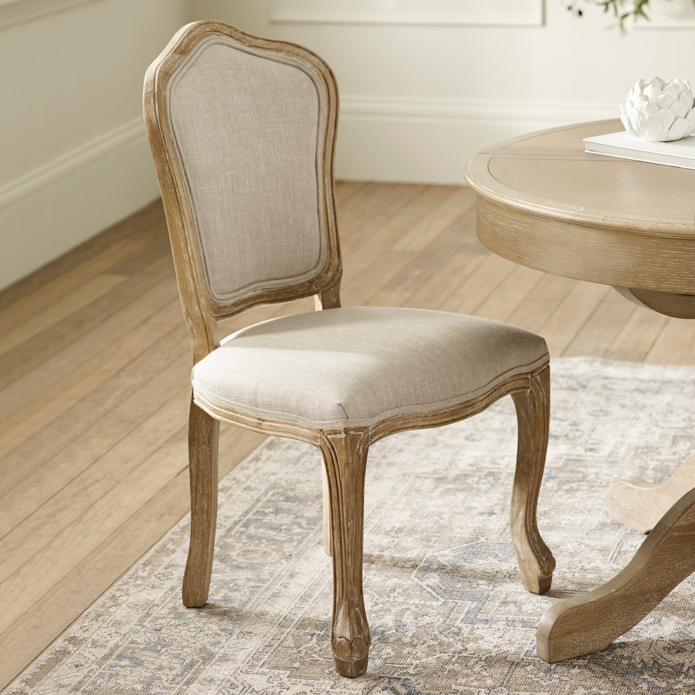 Beige upholstered dining chair beside round wooden dining table in light room setting