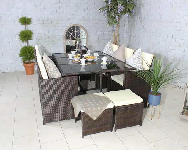 Brown rattan dining set with cream cushions and glass table, arranged with breakfast setting indoors