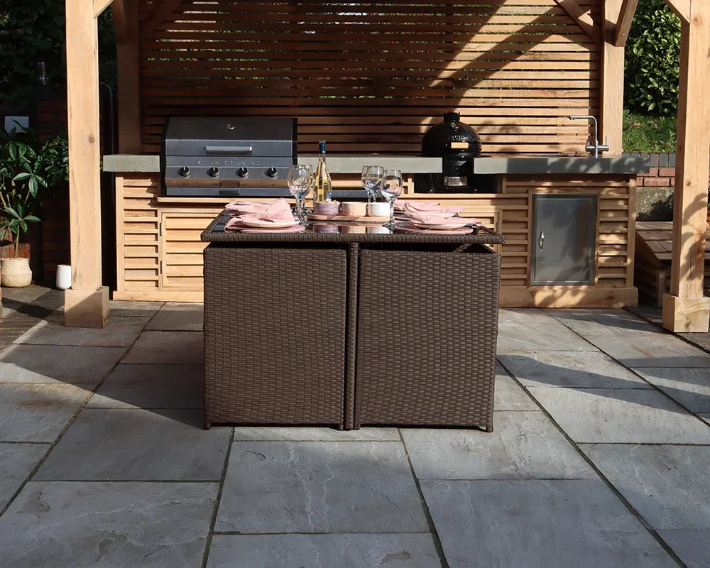 Brown rattan garden dining table set with two cube chairs on patio near outdoor kitchen