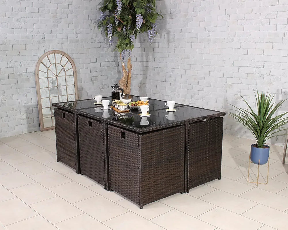 Brown rattan garden dining table set with glass top, cups, and snacks in a tiled room