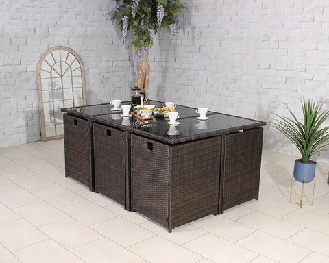 Brown rattan outdoor dining set with glass tabletop and four cube seats in tiled patio space