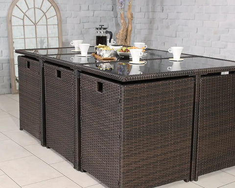 Brown rattan garden dining set with glass tabletop and stools indoors