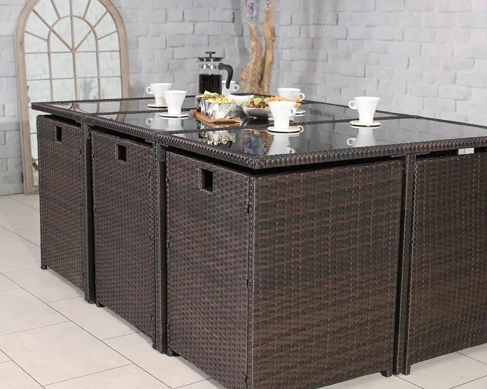 Brown rattan garden dining set with glass tabletop and stools indoors