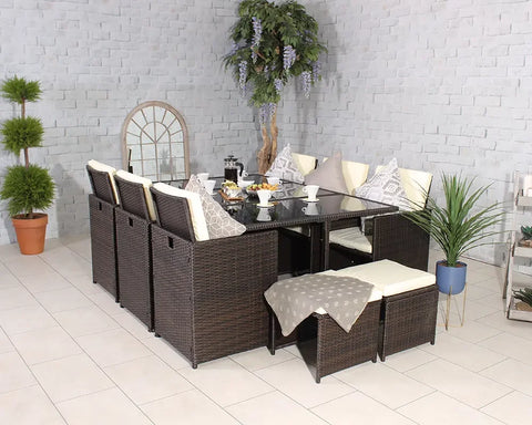 Brown rattan dining set with glass table, cream cushions, and stools in a tiled room