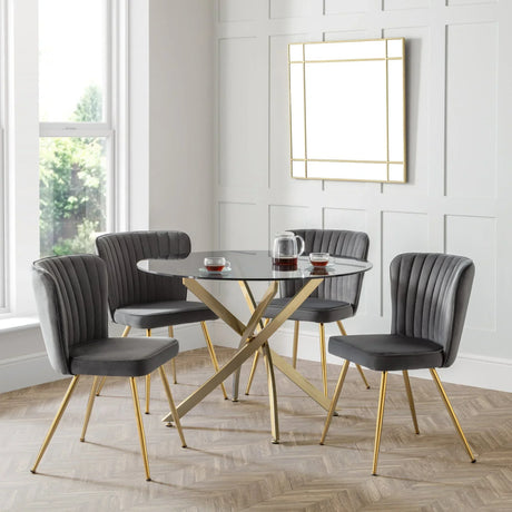 Round glass dining table with gold legs and four grey velvet chairs in modern room