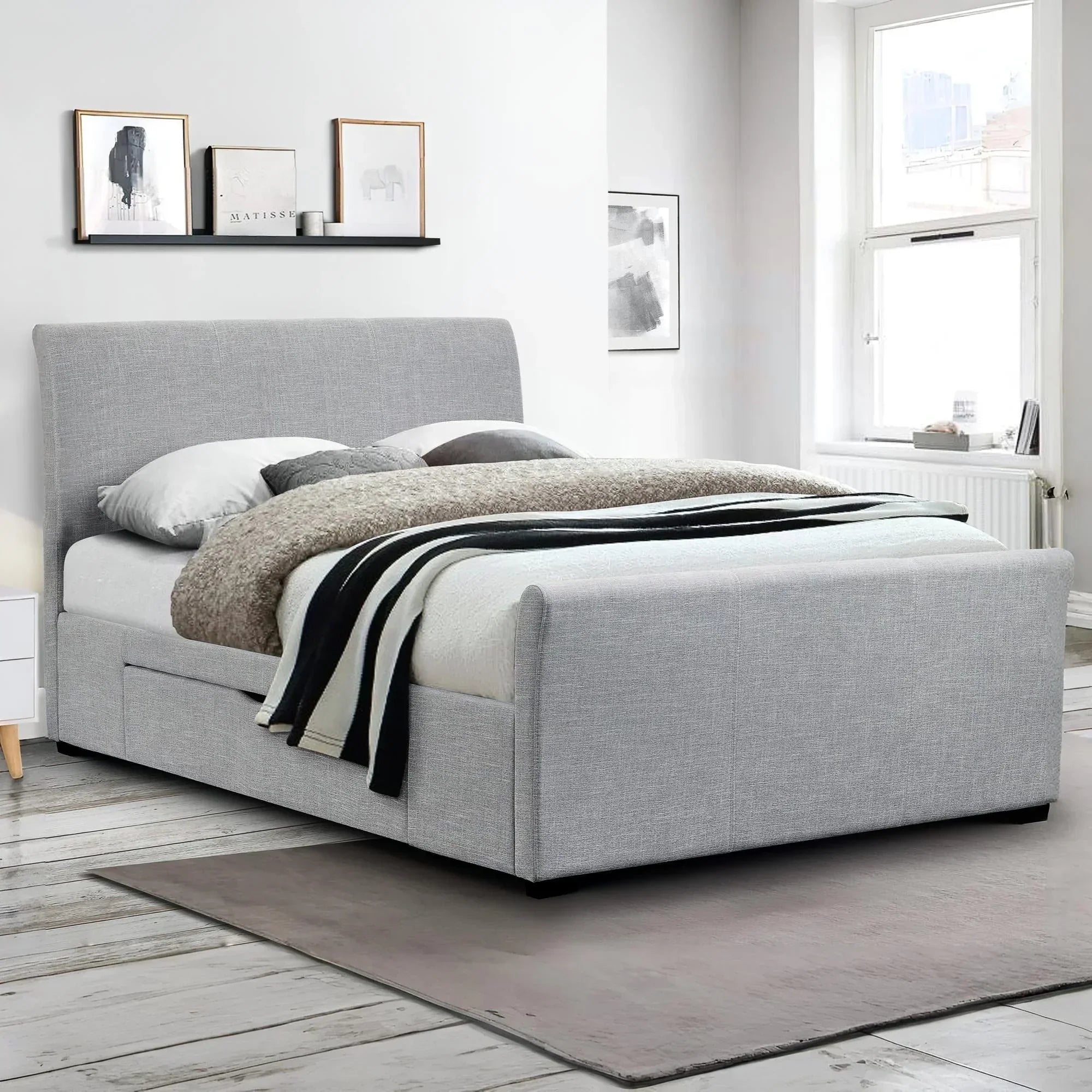 Light grey upholstered double bed with storage in modern bedroom with artwork and window
