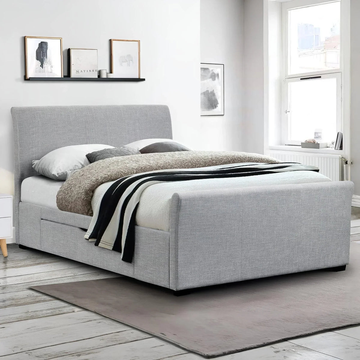 Light grey upholstered double bed with storage in modern bedroom with artwork and window