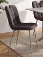 A dark brown tufted upholstered dining chair with slim silver metal legs, shown in a modern dining room setting next to a table on a textured rug.