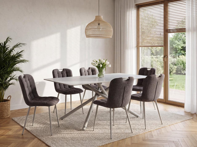 A modern dining set featuring a white rectangular table with a sculptural metal base and six tufted gray upholstered chairs, styled in a bright, contemporary dining room.