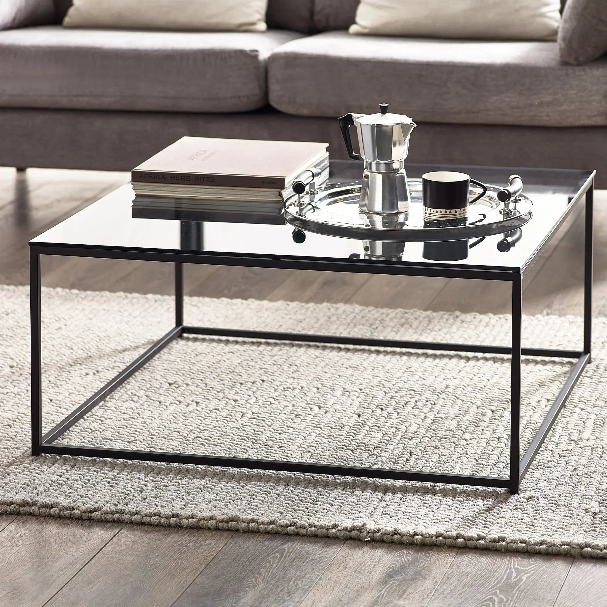 Chicago square coffee table with glass top and black metal frame on light woven rug
