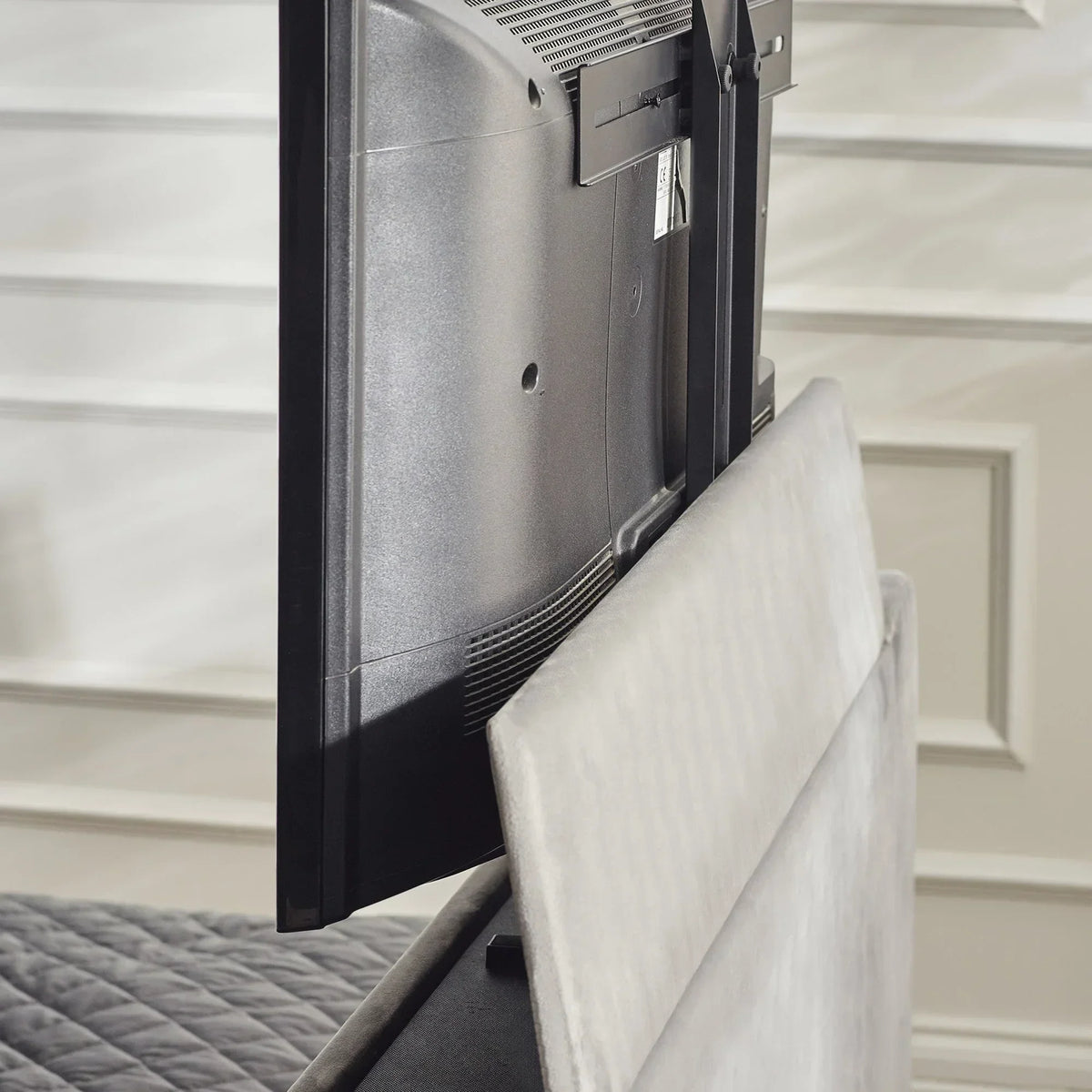 Side view of TV lift bed mechanism with grey upholstered headboard and mounted television