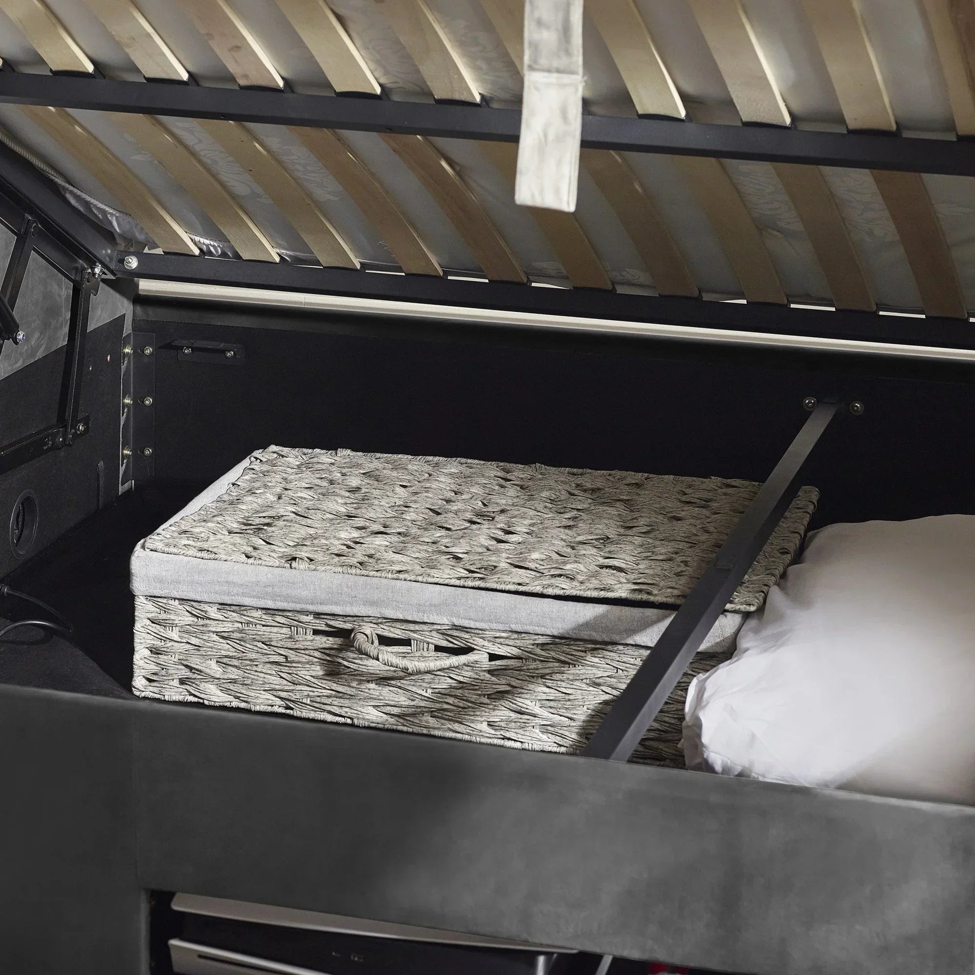 Ottoman storage bed open with grey wicker basket and pillow inside storage compartment