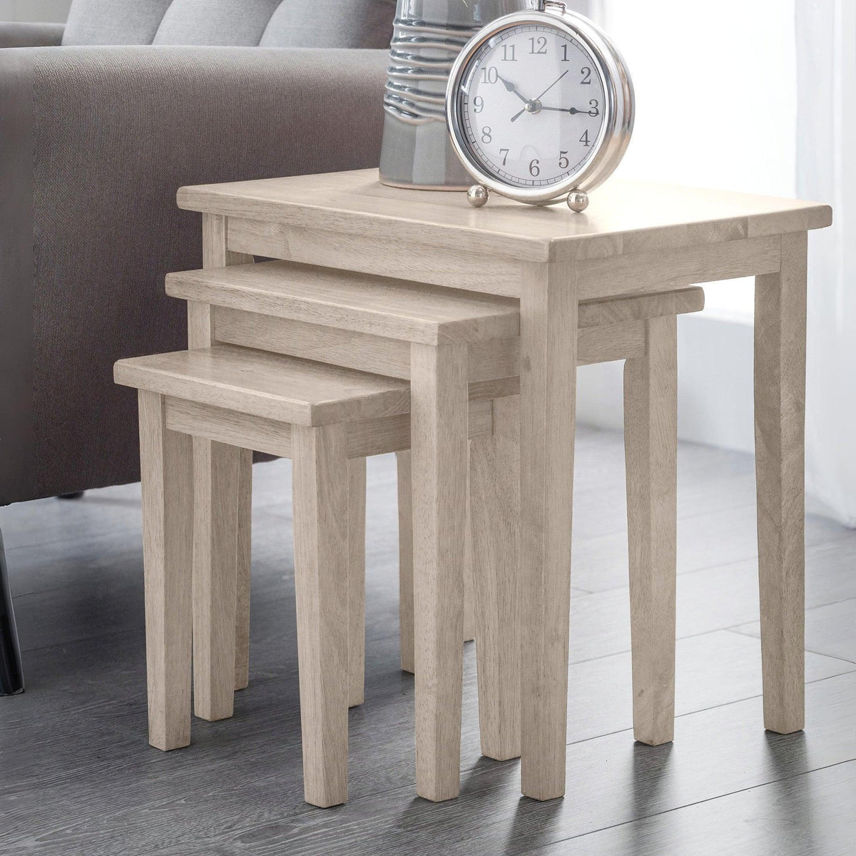 Light oak nest of tables in living room, styled with tabletop clock and ceramic vase