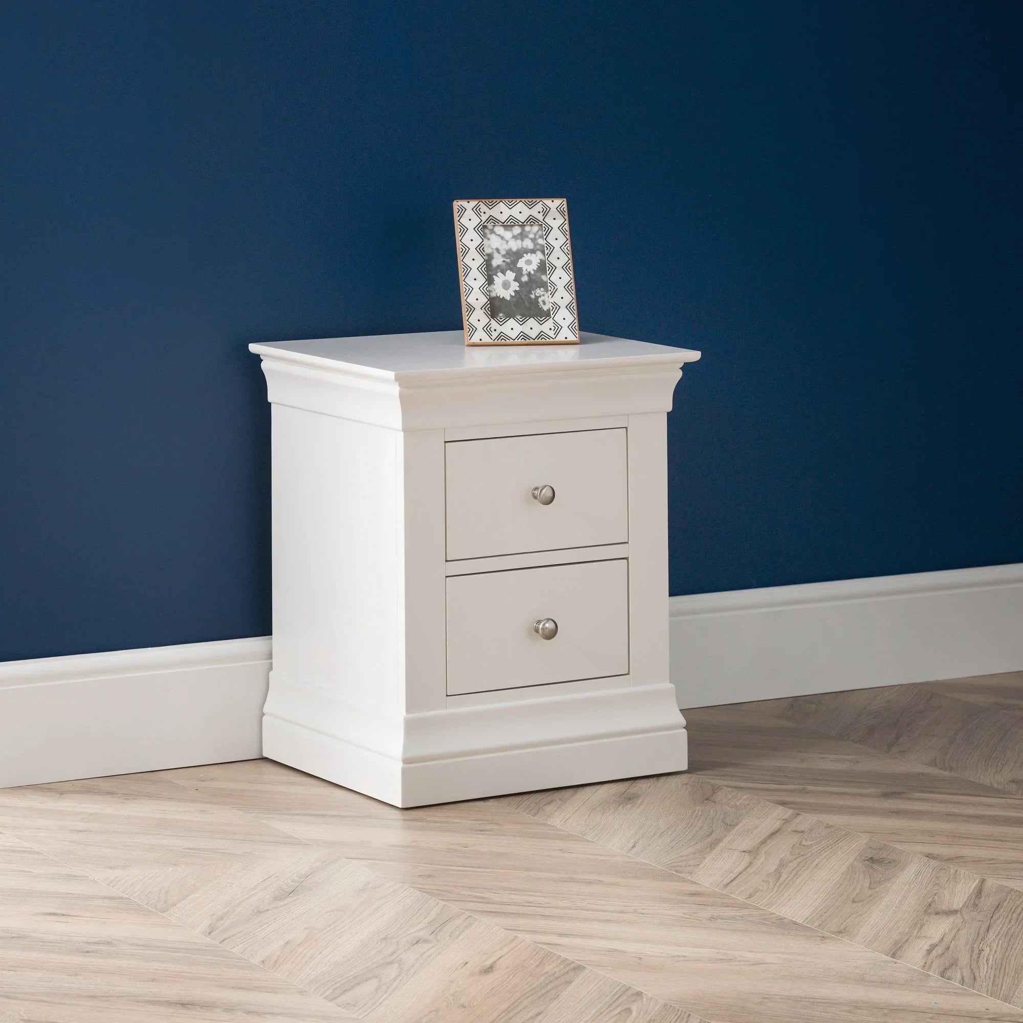 White two drawer bedside table with photo frame against blue wall on wood flooring