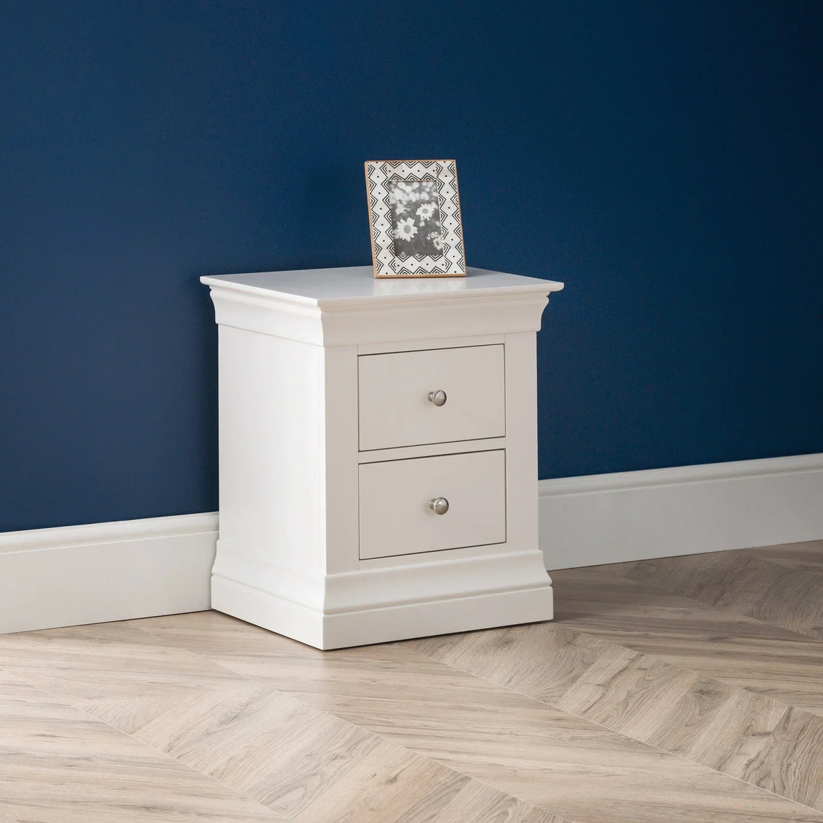 White two drawer bedside table with photo frame against blue wall on wood flooring