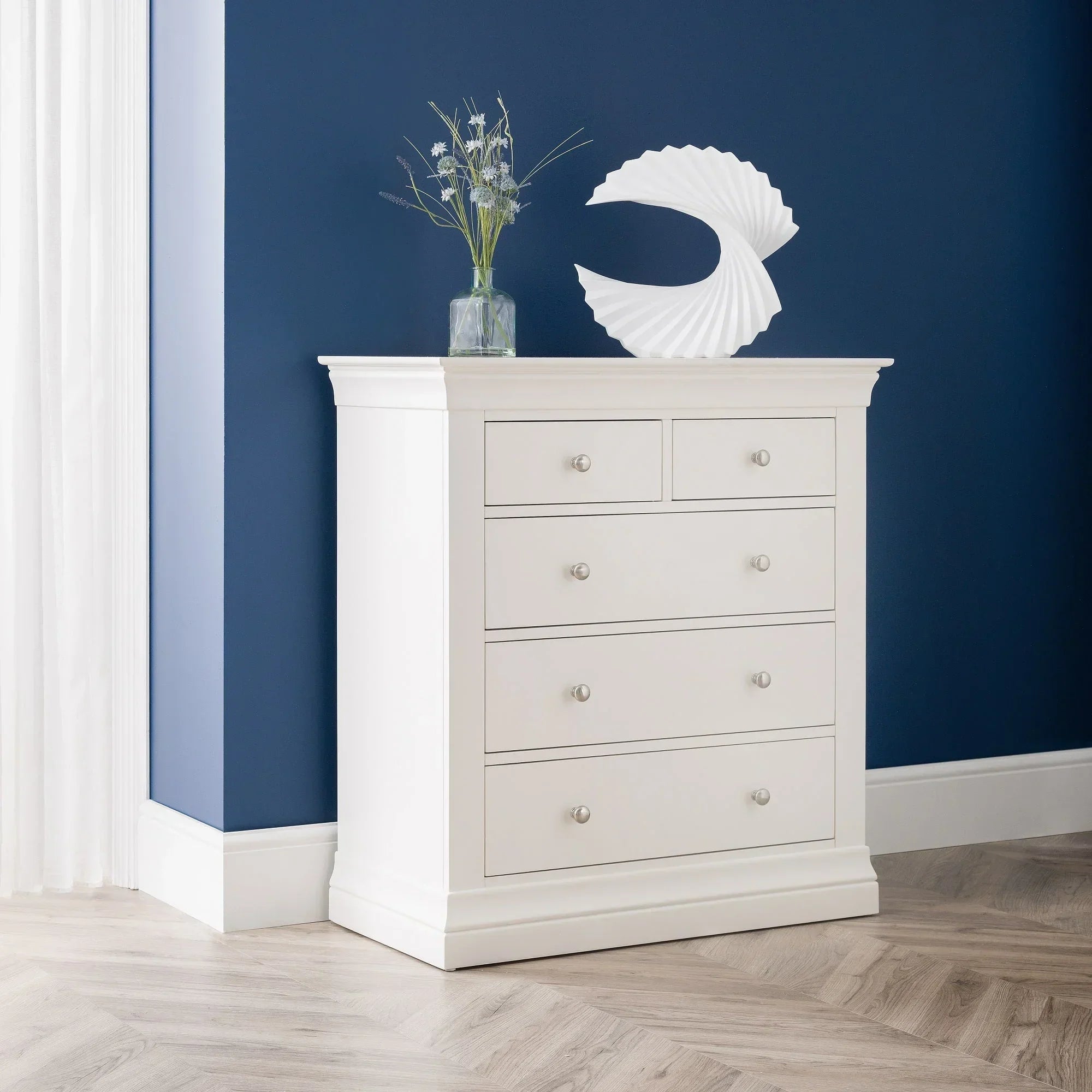 White 3 and 2 drawer chest with silver handles against navy wall, styled with vase and decor