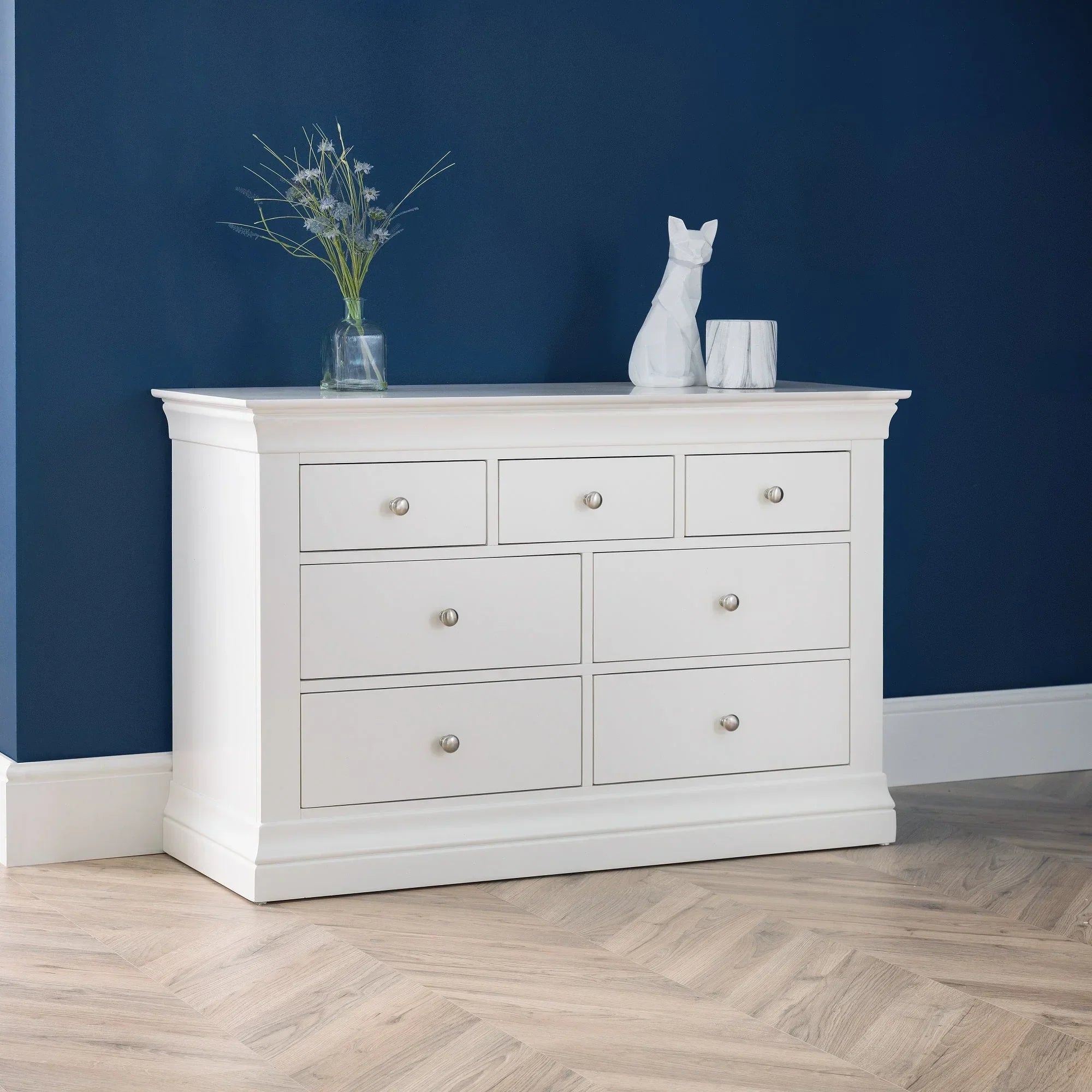 White 4 plus 3 drawer chest with silver handles against dark blue wall and wood floor