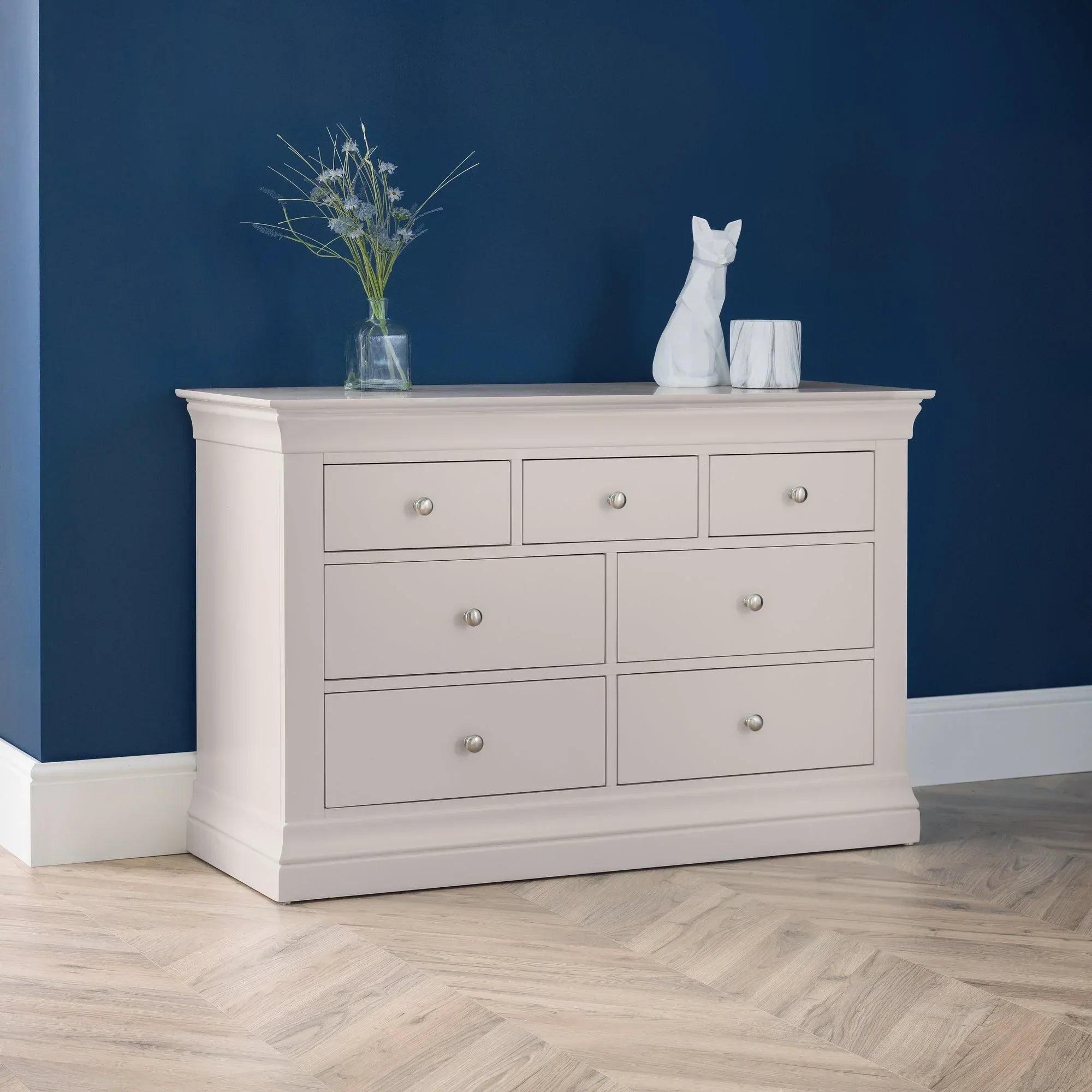 Light grey 7 drawer chest in modern room with blue wall, decorative vase and figurine on top