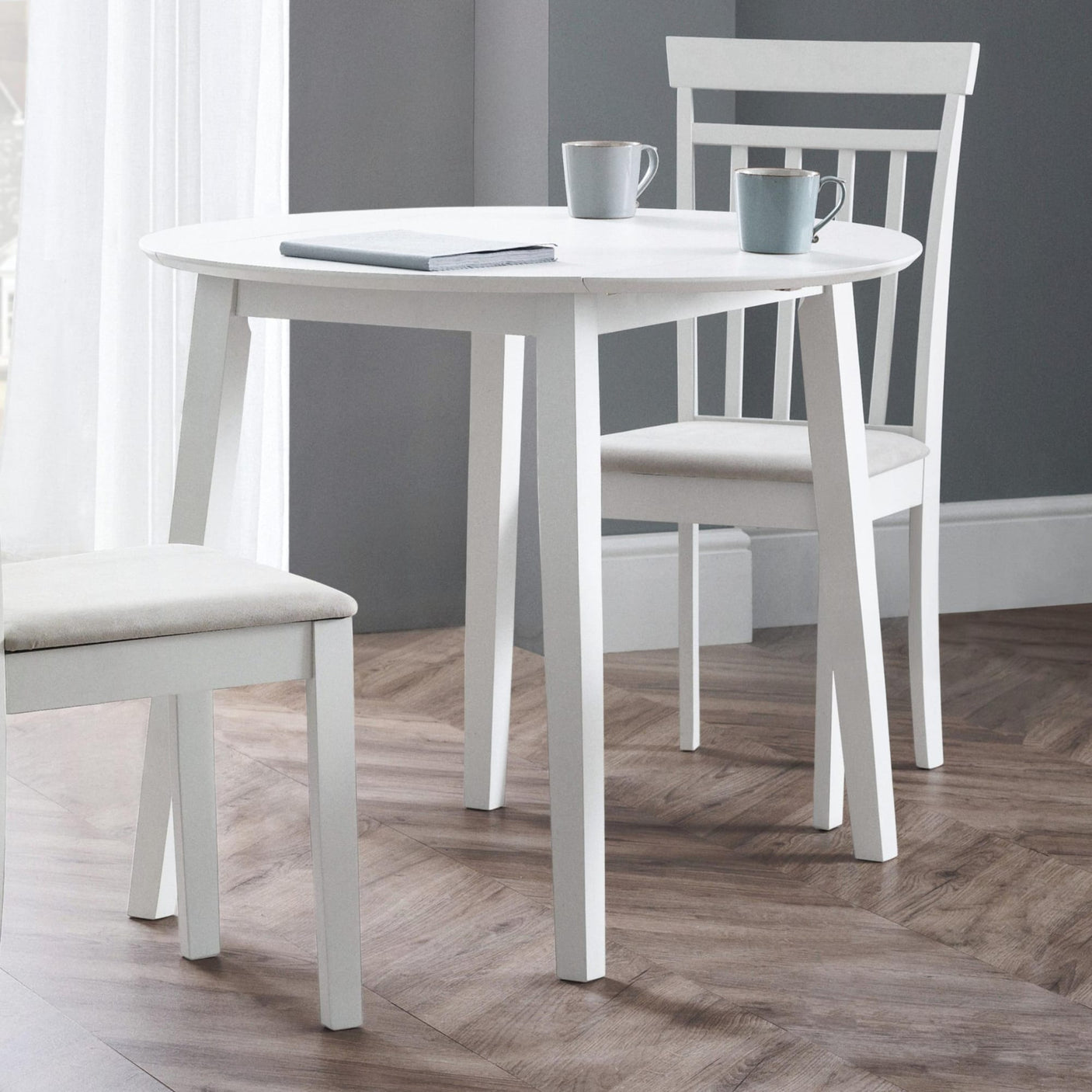 White round Coast dropleaf table with one leaf dropped, two white chairs, wood floor, grey walls
