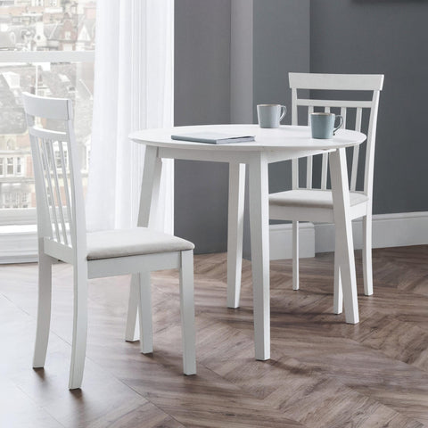 Set of white wooden chairs and round table in a room with wood flooring and window view.