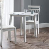 Round white wooden table with both leaves down and three matching chairs in room