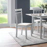 Light grey wooden dining chairs with vertical slats and cream cushioned seats near white table