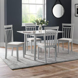 Square white dining table with four white chairs with beige seats on grey rug and wood floor in dining room.