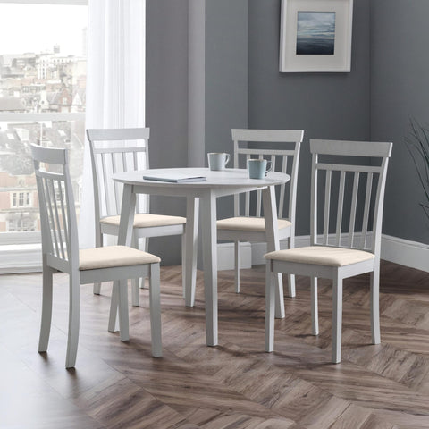 Rectangular white dining table with four white dining chairs with beige seats on wood floor and grey walls.