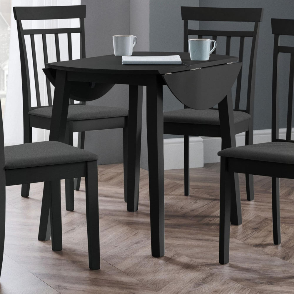 Black drop-leaf table with two matching chairs in a room with wood flooring and gray walls
