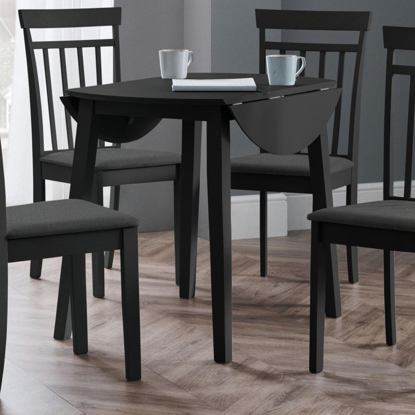 Black drop-leaf table with two matching chairs in a room with wood flooring and gray walls