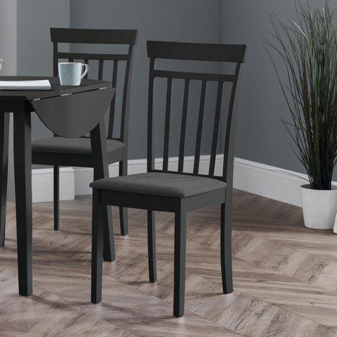 Two black wooden dining chairs with vertical slats and dark fabric seats beside a black drop-leaf table