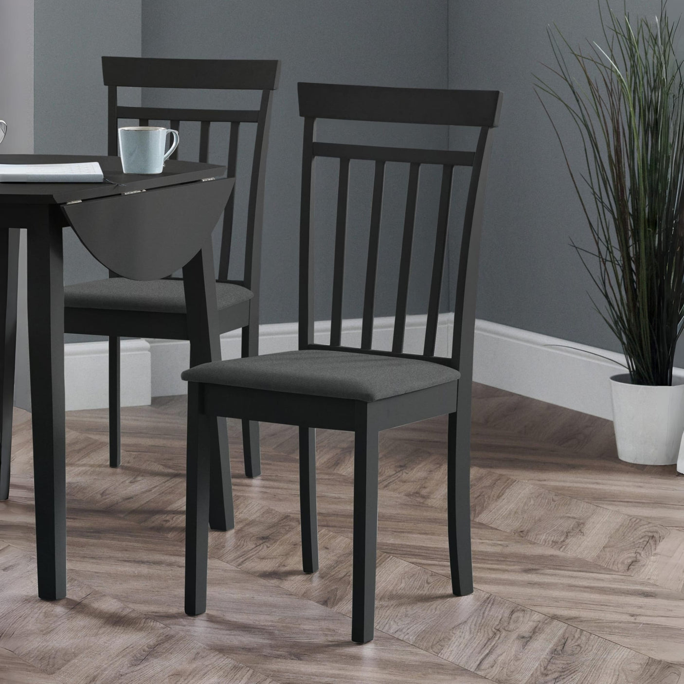 Two black wooden dining chairs with vertical slats and dark fabric seats beside a black drop-leaf table