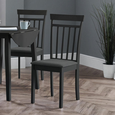 Two black wooden dining chairs with vertical slats and dark fabric seats beside a black drop-leaf table