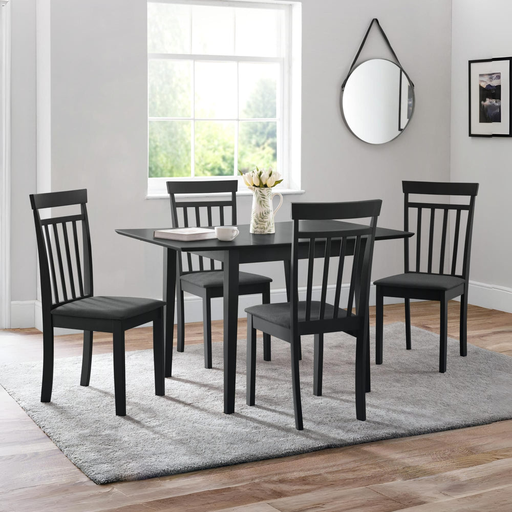 Square black dining table with four black wooden chairs with dark grey cushions on grey rug in room