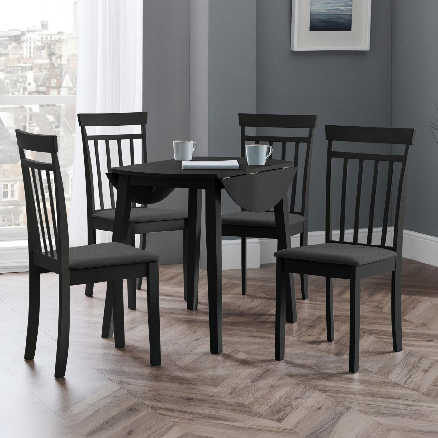 Black dining table with drop leaf and four black wooden chairs with dark grey cushions in room