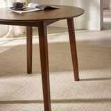 Side view of round brown wooden table with drop leaf folded down on beige rug with angled legs visible