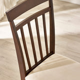 Close-up of dark wood dining chair back with vertical slats and beige cushioned seat on light floor